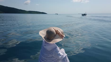 Mujer-Turista-Con-Sombrero-De-Verano-Sentada-En-El-Borde-De-Un-Barco-Y-Señalando-Con-El-Dedo-Hacia-Adelante