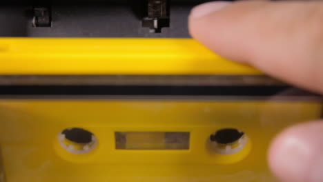 inserting a yellow cassette tape into a deck, closing the cover, pressing play