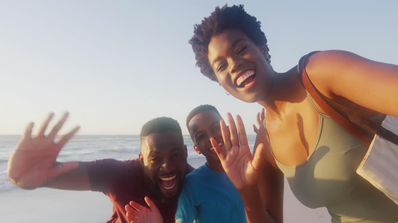 video de una feliz familia afroamericana haciendo una videollamada en la playa al atardecer