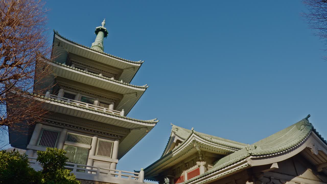 A low-angle view of the majestic pagoda and traditional roof of the Tokyo Metropolitan Memorial Hall against a clear blue sky