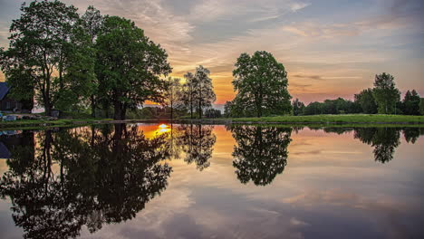 Sunrise-reflecting-on-calm-lake-near-private-homestead,-time-lapse