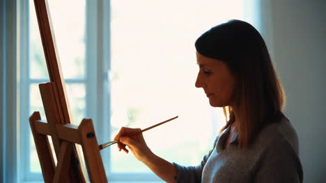 woman painting at an easel by a window