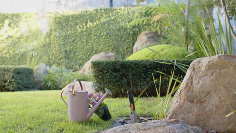 watering can and gardening tools on grass in garden, ready for planting flowers