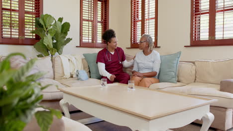 caregiver comforting senior woman on sofa at home, sharing warm embrace