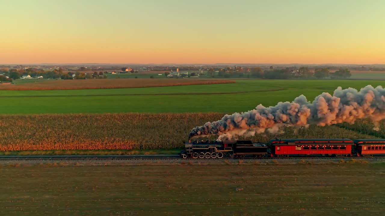 vista aérea de un motor de vapor y automóviles de pasajeros en el amanecer dorado con una cabeza llena de vapor y humo que viaja a través de las tierras de cultivo