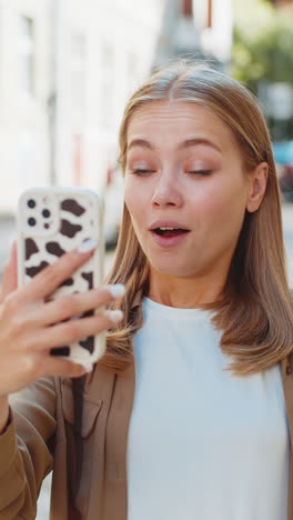 excited happy joyful winner young woman using smartphone looking at screen standing on city street