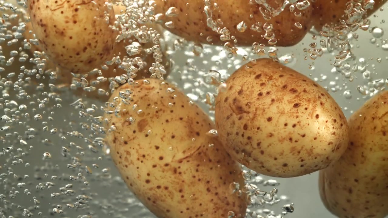Patate fresche che si immergono in acqua bollente con bolle.