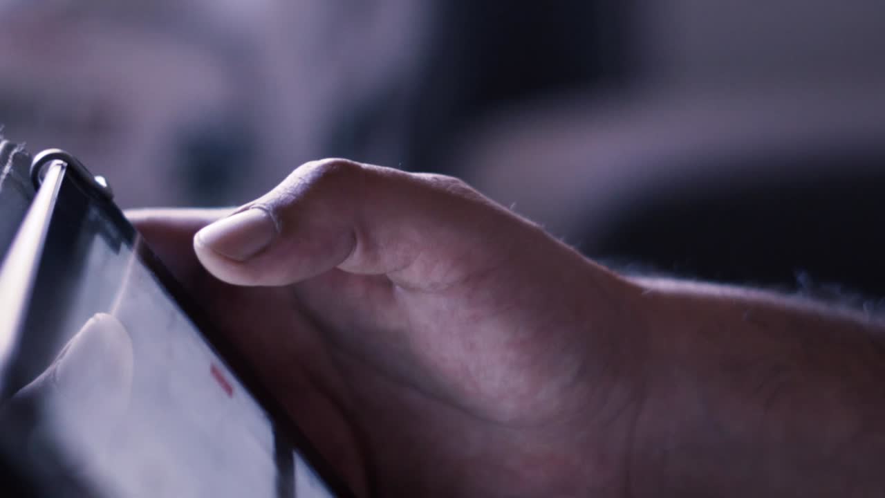Shooted in slow motion showing man's hands browsing social media or playing with a mobile tablet at evening (dark space)