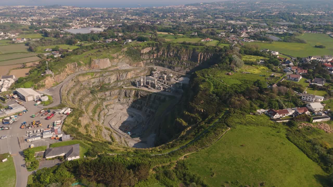 High drone shot overhead and descending into Les Vardes Quarry Guernsey showing quarry, equipment and surrounding area on bright sunny day