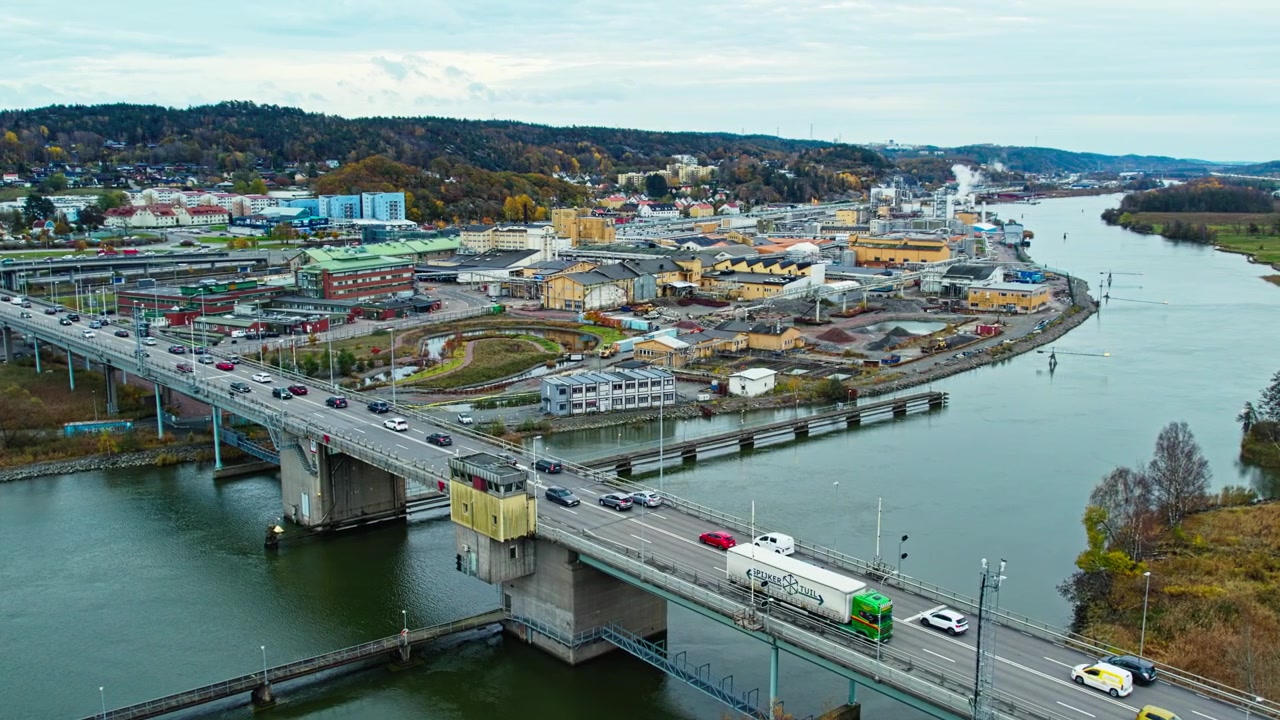 Veduta aerea con drone del ponte Jordfallsbron che attraversa il fiume Göta älv in Svezia. Il traffico intenso si muove lungo l'autostrada mentre edifici industriali costeggiano la riva del fiume sotto un cielo autunnale.