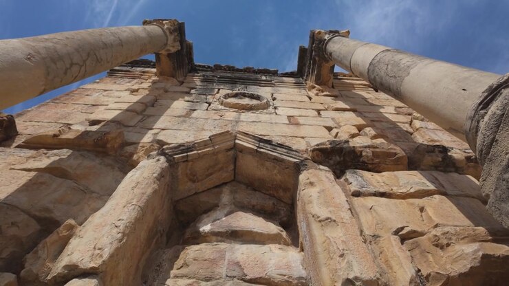 Inquadratura dal basso a livello del terreno dell'Arco di Trionfo di Caracalla a Volubilis, che evidenzia la muratura romana in pietra, le colonne monumentali e l'artigianato architettonico classico nel sito Patrimonio dell'Umanità UNESCO del Marocco.