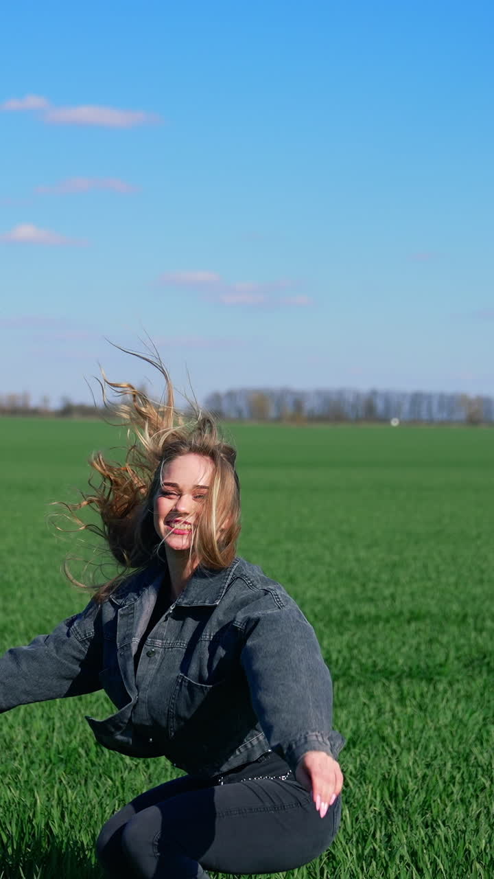 Happy girl in jeans on a green meadow. Beautiful young woman jumping joyfully on a field in a bright day. Cheerful model among nature. Vertical video