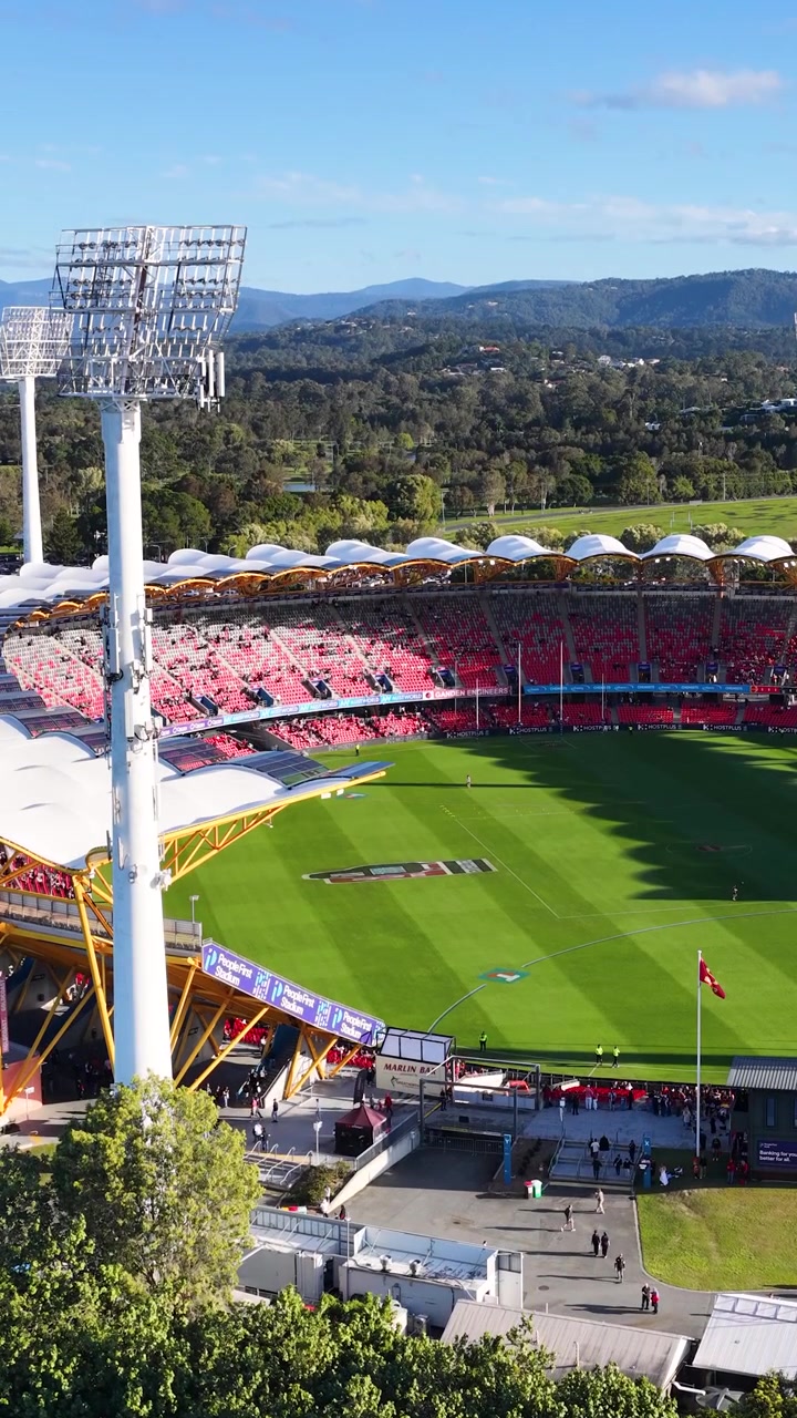 High-angle wide shot of a modern sports arena under bright daylight with surrounding hills.