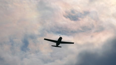 tracking shot showing silhouette of airplane flying against sunlight and dark clouds at sky.