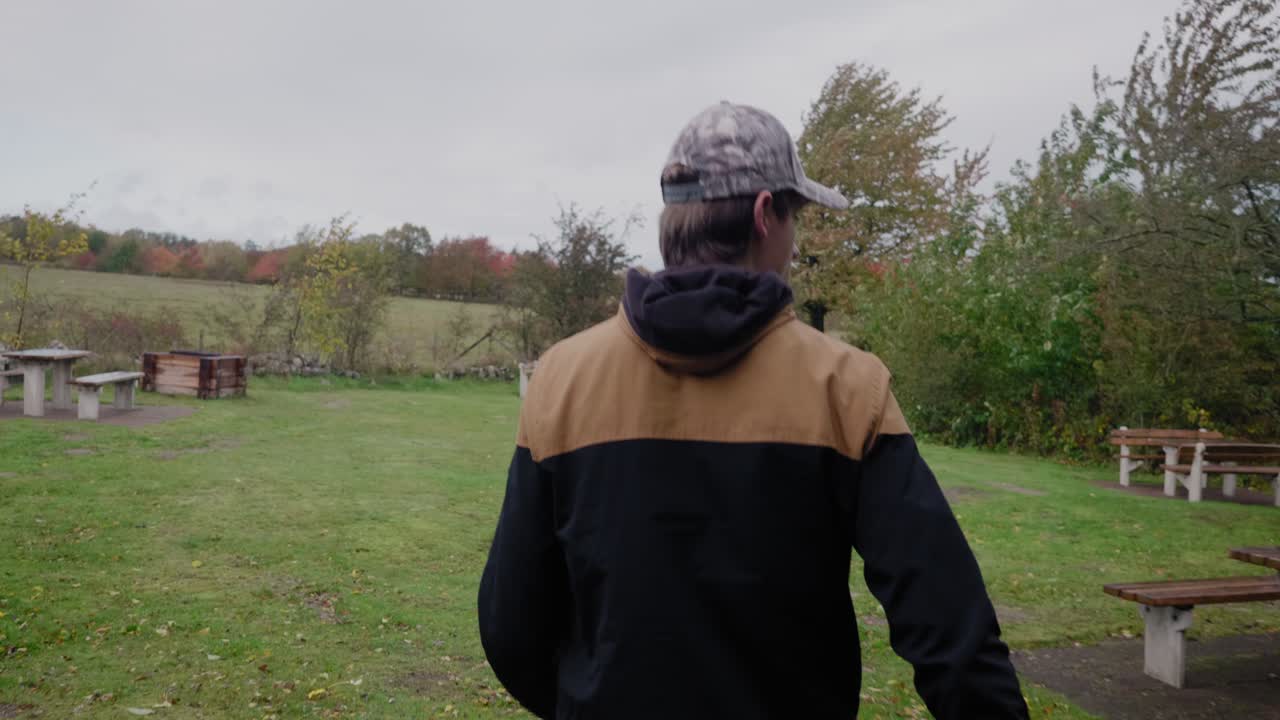 젊고 키가 큰 스칸디나비아 남자는 주머니에 손을 넣고 벤치와 함께 휴게소를 걸어 다니며 탐색, simrishamn, 스웨덴 vårhallarna - 추적 및 패닝 중간 샷