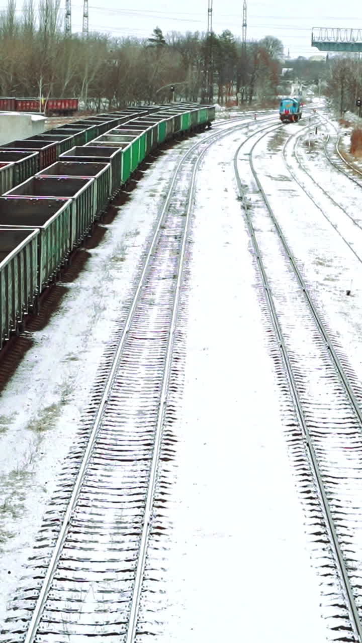 Aerial view on a huge number of iron containers of different colors located at the final station on the background of a freight train, which is moving in their direction. Close-up. Vertical video