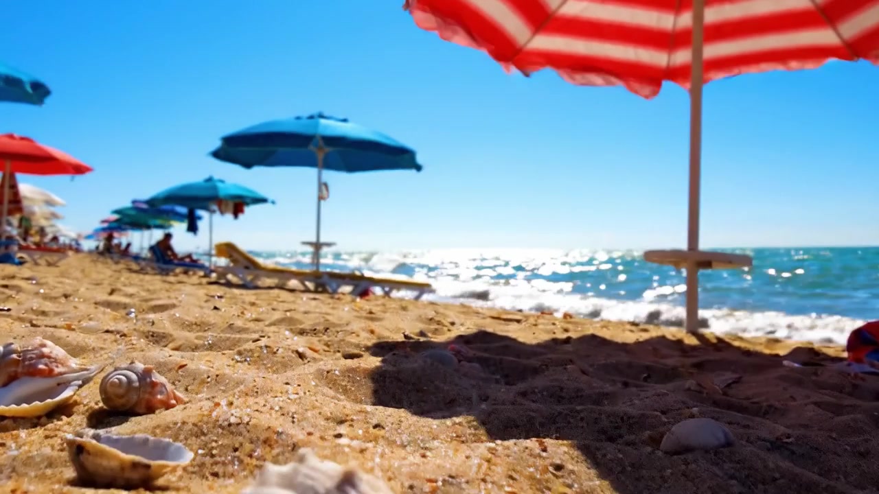 Una tranquilla scena da spiaggia con ombrelloni colorati, conchiglie vivaci e onde oceaniche scintillanti sotto un cielo azzurro limpido