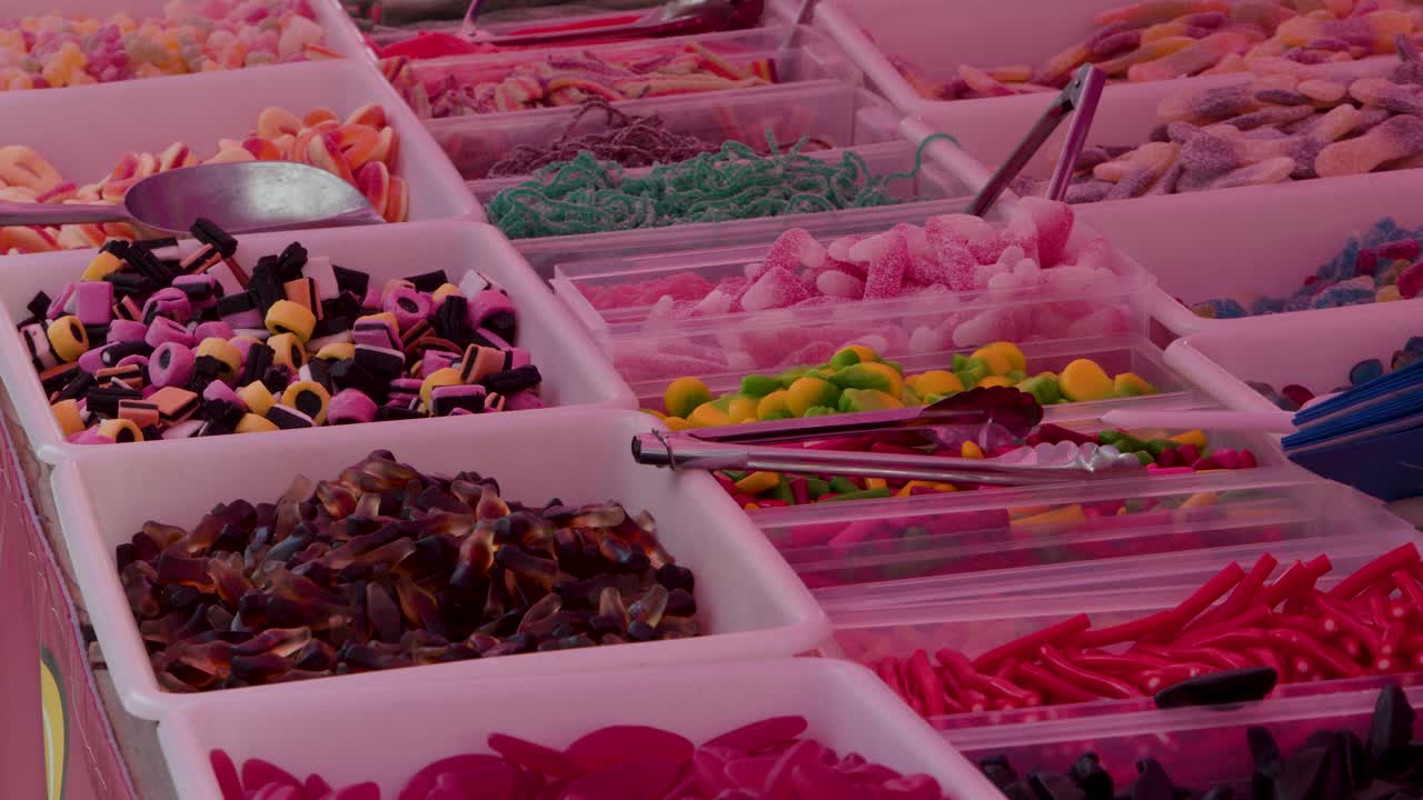 Assorted colorful candies displayed in bins at outdoor market, natural daylight, slight camera pan