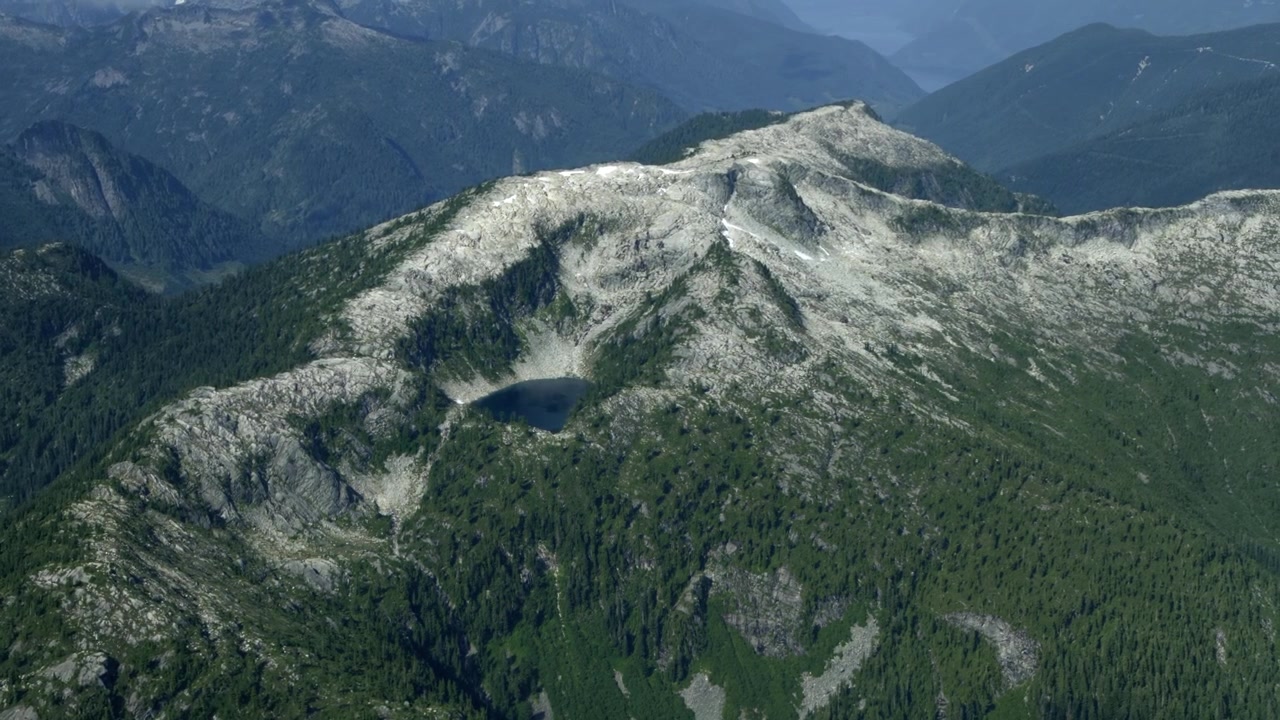 Alpine Tarn Lake Nestled High Within Rocky Mountain Ridge In Canada. - aerial shot