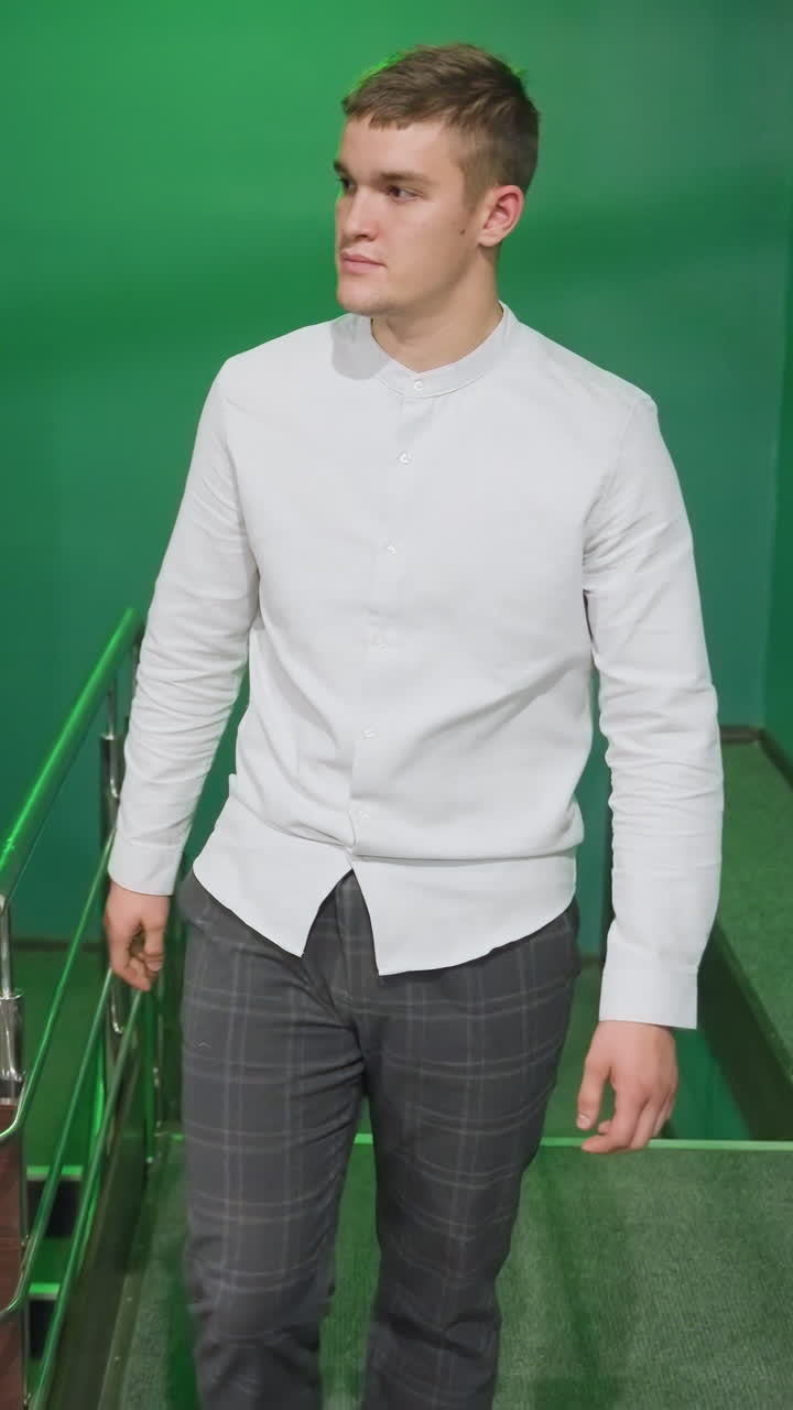 셔츠와 바지를 입고 계단을 올라 빌리어드 방으로 들어가는 남성의 전면 촬영. 녹색 조명은 주변에 독특한 빛을 습니다. 자신감있는 표정과 캐주얼한 걸음