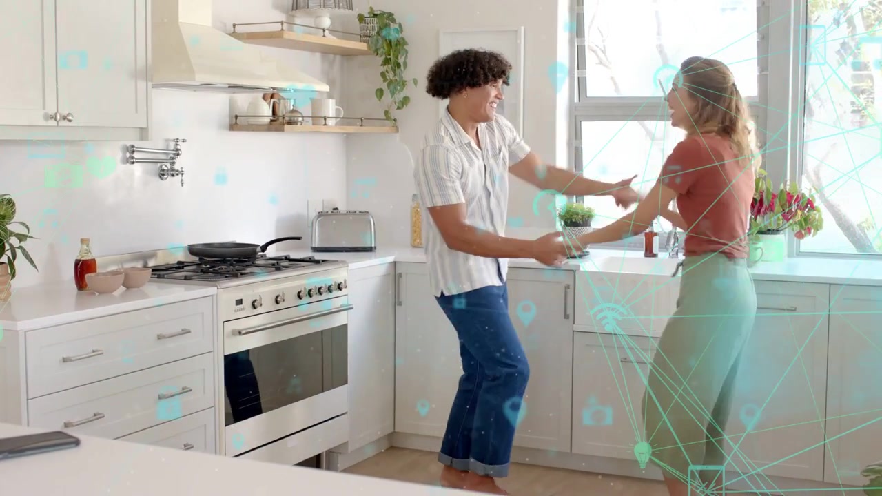 Man and woman reaching hands, dancing in kitchen, playing while tech overlay hovering heart icons