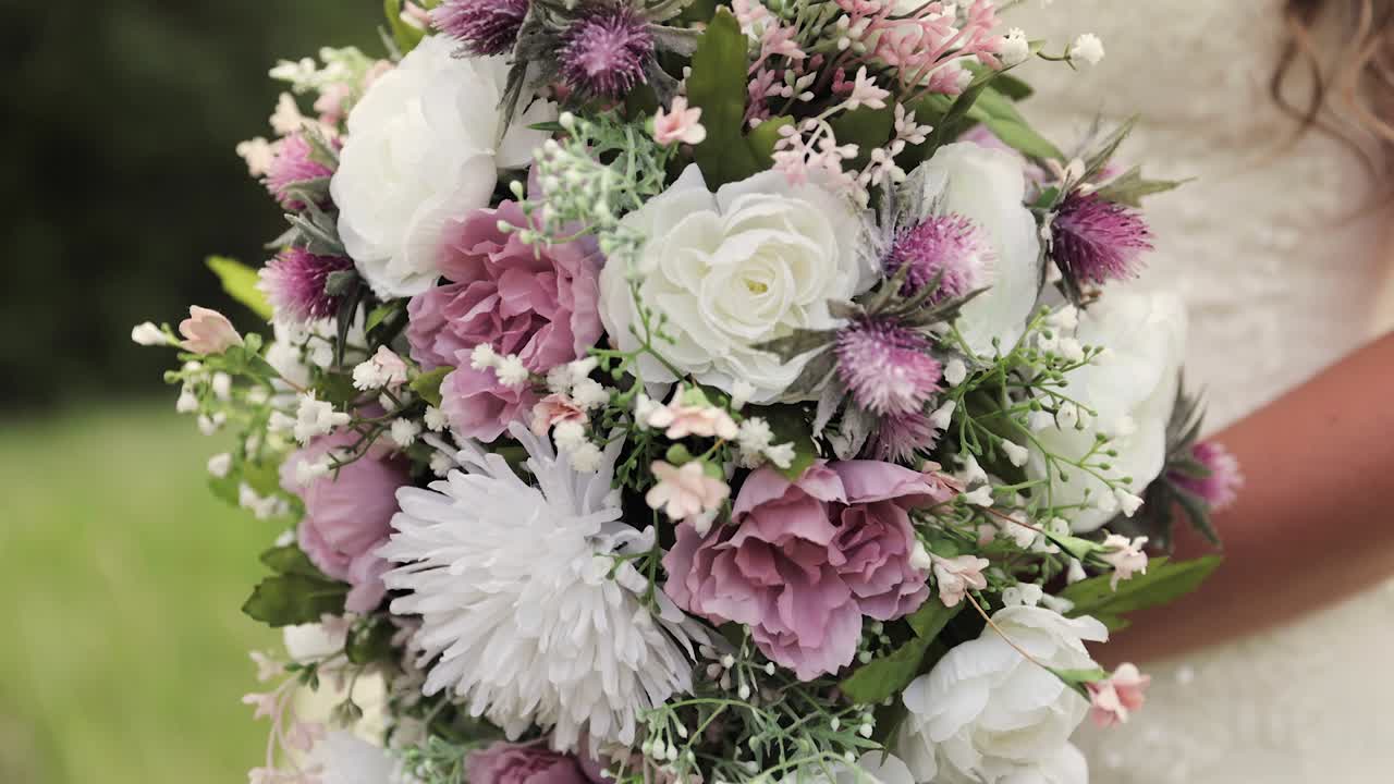 1080p 60fps 야외에서 손에 분홍색과 흰색 꽃다발을 들고 있는 웨딩 드레스를 입은 신부 클로즈업