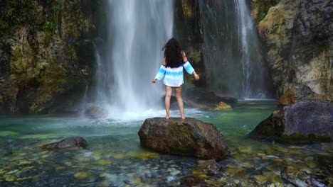 girl enjoying freshness of waterfall droplets standing on cliff, beautiful spot in theth, albania