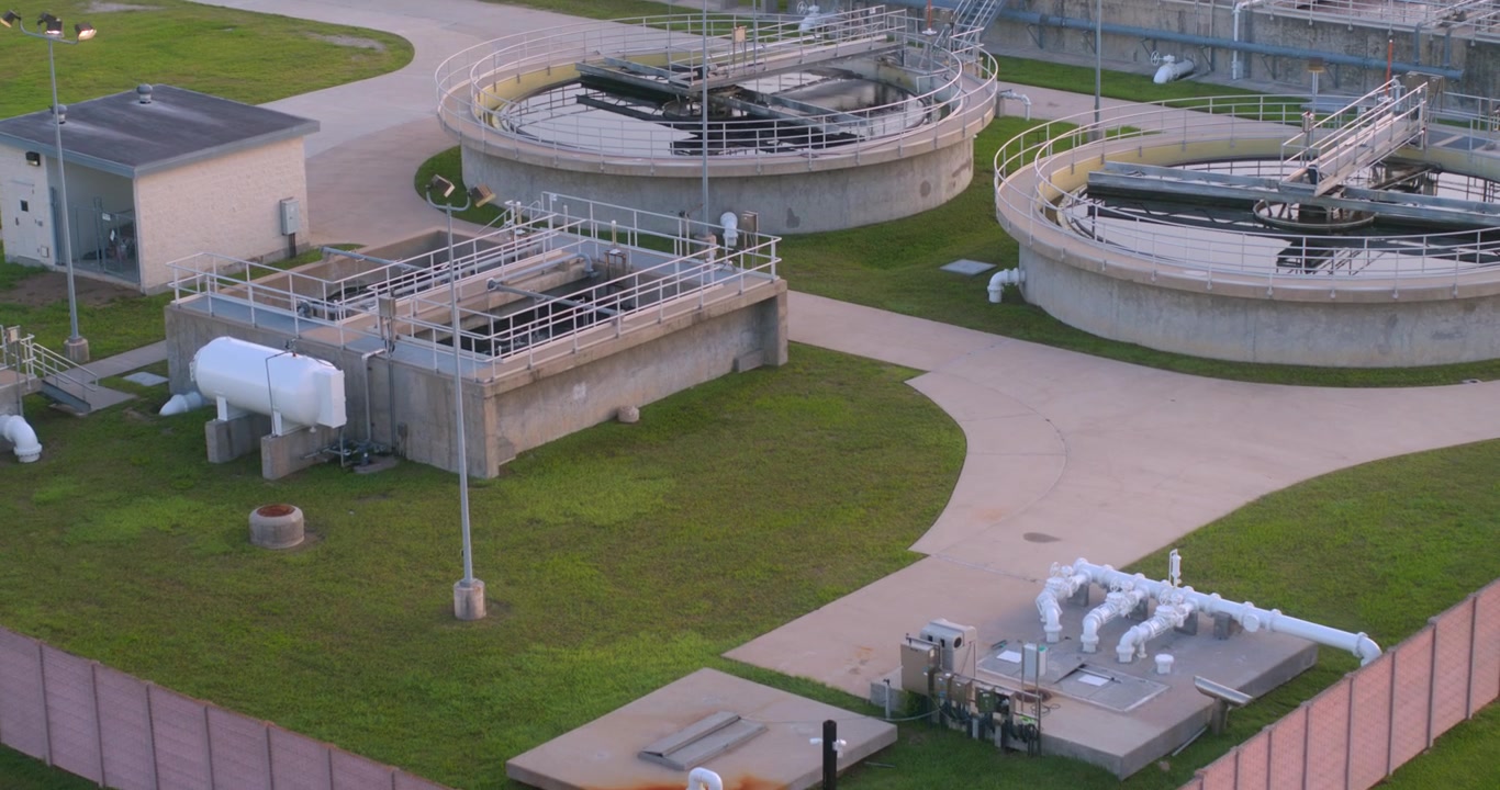 Denne fugleperspektiv droneudsigt fanger et spildevandsrenseanlæg direkte ovenfra, der viser den geometriske udformning af klaringsbassiner, beluftningsbassiner, bundfældningstanke og anden industriel infrastruktur