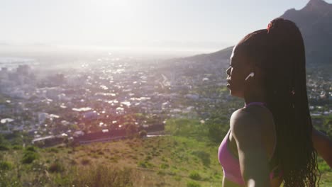 african american woman wearing wireless earphones stretching her arms outdoors