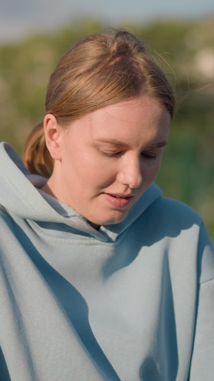 Young lady engaging in fitness exercise while kneeling forward, hair tied back, with blurred background featuring tree and unclear figures in the distance