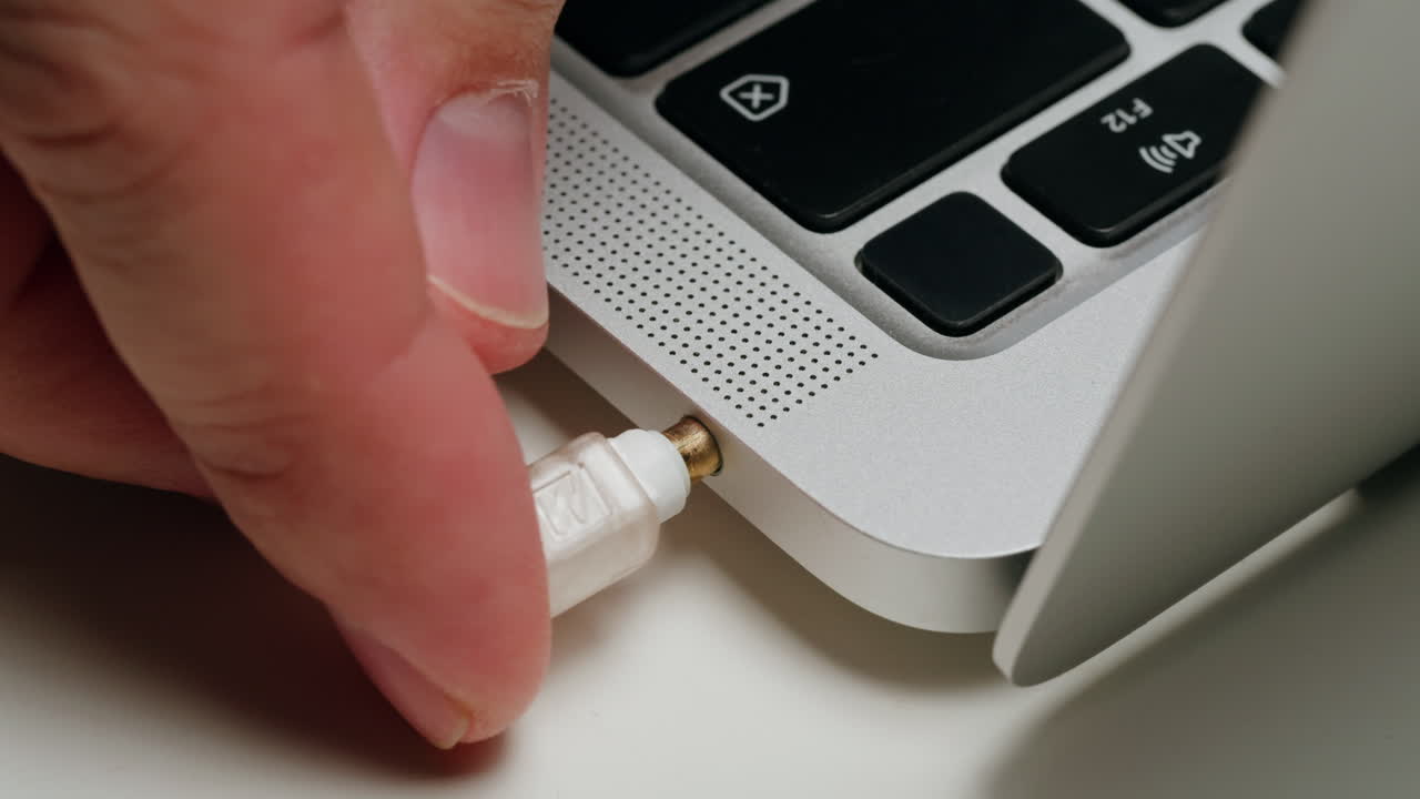 Hand plugging in a headphone cable to a laptop