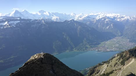 Man-hiking-on-beautiful-ridge-top-amongst-huge-mountains-and-above-a-green-valley-with-a-blue-lake-and-taking-in-the-view