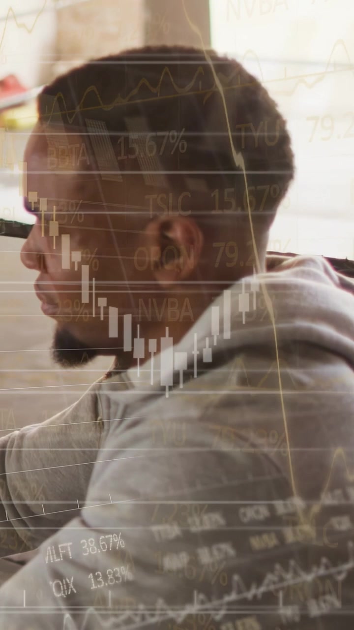 Vertical video: Man sitting desk monitoring finance data updating watching charts layering over him