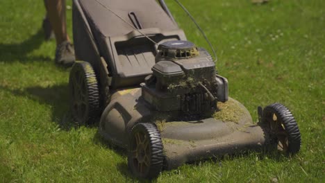 close up tracking shot of male person mowing lawn with old mower during sunny day - 4k low angle - working in own garden