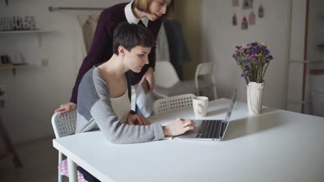 Young-woman-sitting-at-table-and-making-note-in-notebook.-Woman-using-laptop