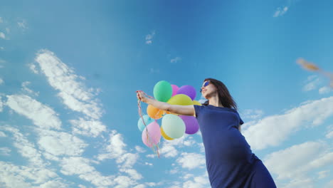 happy pregnant woman playing with balloons against the blue sky