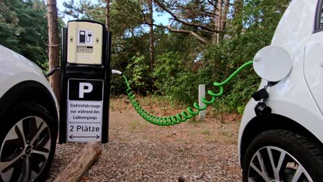 two white ev cars plugged into a public charging station in a forest