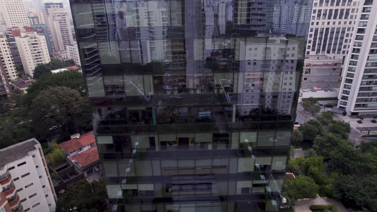 el dron sube frente a una torre comercial reflejada mientras el paisaje de los edificios de são paulo se revela en el fondo