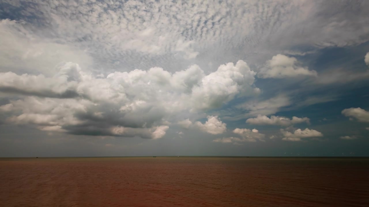 Clouds fill the sky above Con Nhan Beach in Vinh Long, Vietnam. The view shows the coastline and distant water. The weather looks changeable as clouds shift.