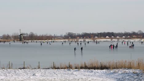 People-ice-skating-on-a-frozen-lake-past-a-windmill-on-a-sunny-winter-day-in-the-Netherlands-during-the-pandemic