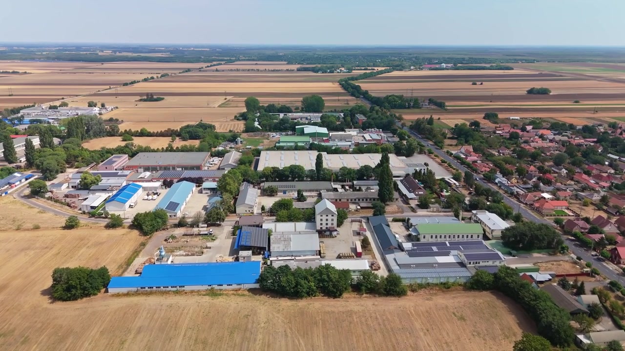 Hajdúböszörmény, Ungheria: distretti industriali e residenziali con fabbriche, magazzini, strade e terreni agricoli circostanti in un'ampia panoramica aerea diurna sotto un cielo limpido