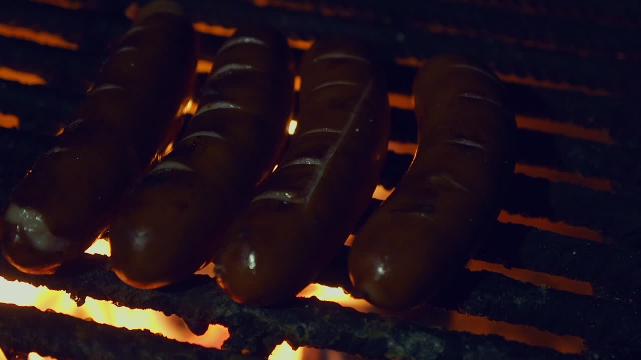 escena muy oscura: salchichas bratwurst cocinar en la parrilla de fuego en la noche oscura