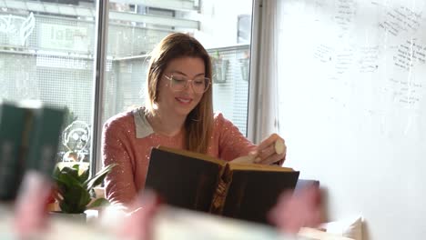 woman in glasses smiling while reading a book