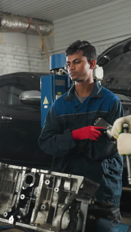 un ingeniero demuestra cómo soltar un perno mientras los estudiantes toman notas en cuadernos, otro colega observa atentamente en un taller automotriz lleno de maquinaria y motores de automóviles en el fondo