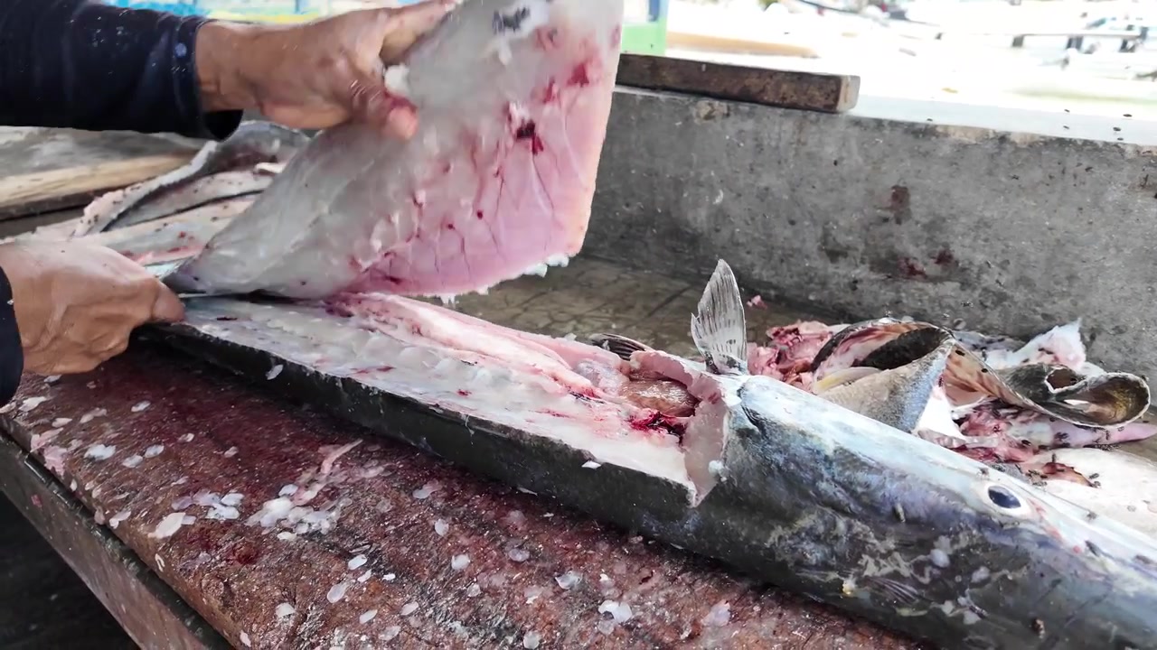 Fischerhände öffnen frischen Barrakuda-Fisch auf einem rustikalen Markttisch