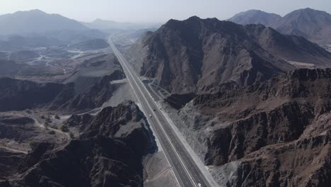 4k:-Rear-drone-view-of-UAE-Mountain-range,-Traffic-movement-in-between-the-Khorfakkan-mountains,-Sharjah,-United-Arab-Emirates