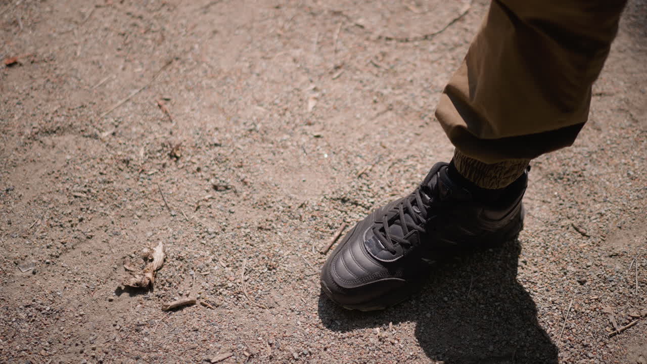 Man Discovers White Pill Beside Bottle On Dusty Path, Closeup Of Sneaker And Khaki Trousers, Sunlight Casts Sharp Shadow, Small Plastic Fragment And Dry Leaf Add Gritty Realism, Scene Suggests