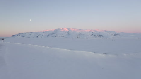 AERIAL:-Snow-White-mountain-with-Pink-sunlight-hitting-the-top-in-Iceland-Winter,-Ice