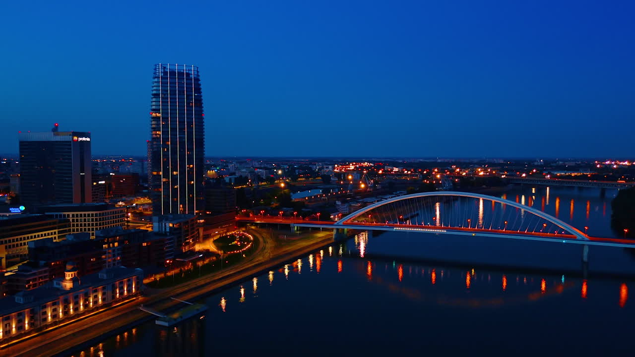 Bratislava skyline illuminated at dusk. The skyline of Bratislava glows with lights as night falls, showcasing modern architecture and the iconic bridge