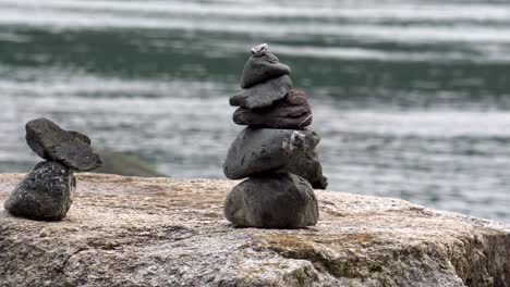 Slow-tracking-shot-of-two-small-cairns-stacked-on-a-boulder-by-the-sea